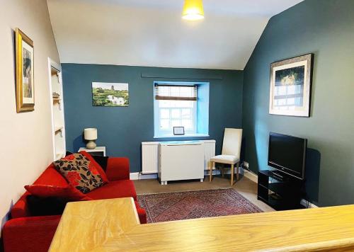 a living room with a red couch and a tv at The Cobbles Inn Apartment in Kelso