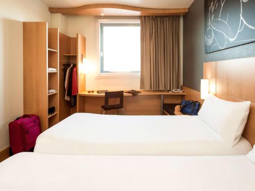 a hotel room with two beds and a desk at Ibis Barcelona Meridiana in Barcelona