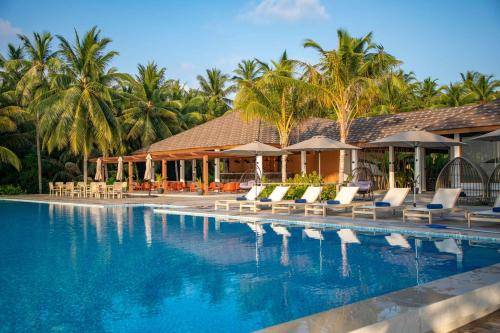 a resort swimming pool with lounge chairs and palm trees at Fiyavalhu Resort Maldives in Mandhoo