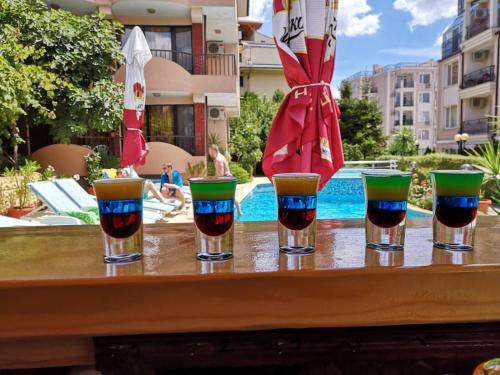 four glasses of wine on a table next to a pool at Family Hotel Rainbow in Sveti Vlas