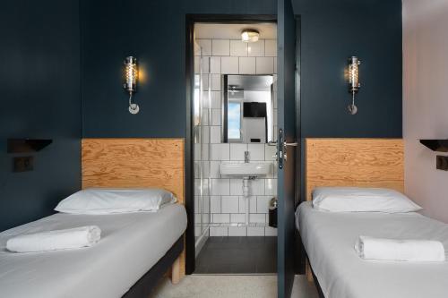 two beds in a room with a bathroom with a sink at Eklo Marne La Vallée in Serris