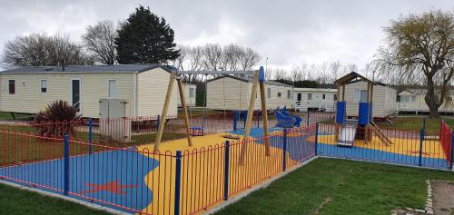 a playground in a park with an orange fence at Bewles Caravan in Rhyl