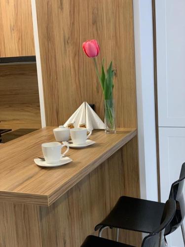 een tafel met twee kopjes en een roos in een vaas bij Apartament Fordon przy Onkologii in Bydgoszcz