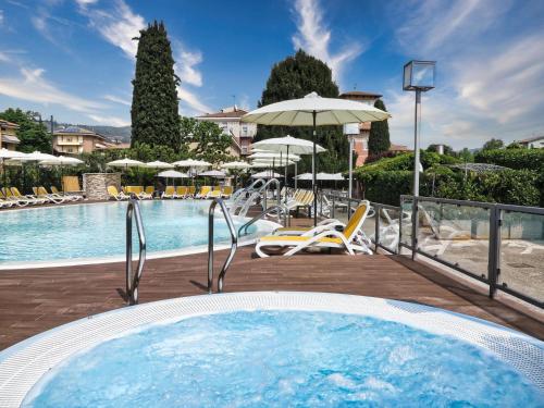 a pool with a hot tub and chairs and umbrellas at Hotel Villa Mulino ***S in Garda