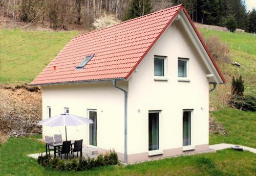 ein weißes Haus mit einem Tisch und einem Regenschirm in der Unterkunft Frankenwald Chalets - Ferienhaus Hans in Wilhelmsthal