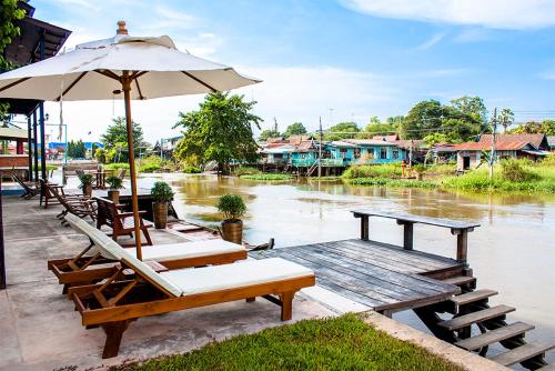 a group of tables and chairs with an umbrella and water at The Bank River House Ayutthaya in Ban Yai (1)