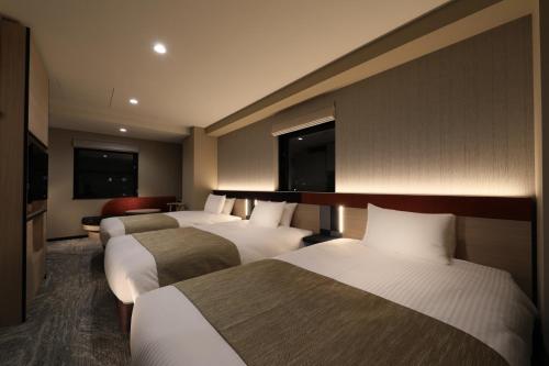東京にあるアルモントホテル日暮里のベッド3台とソファが備わるホテルルームです。