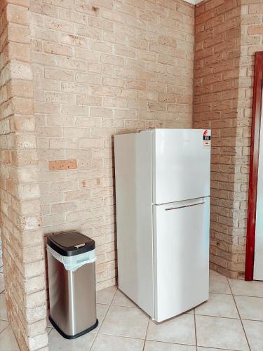a white refrigerator and a trash can next to a brick wall at Carnarvon 3BR & 2BA Holiday House in Carnarvon