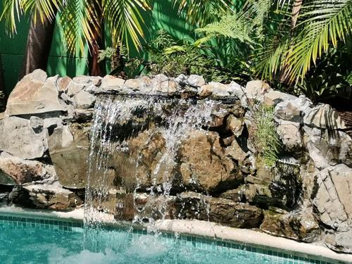 een waterval in een zwembad met een rotswand bij Hostel Antorchas in Dominical