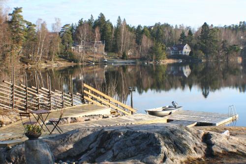 a dock with a boat and a house on a lake at Sjöställe Gudö in Vendelsö