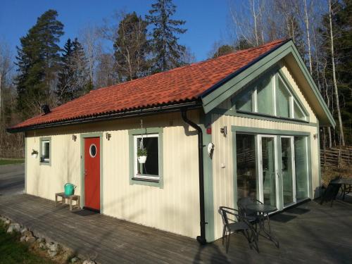 a small white building with a red door and a deck at Sjöställe Gudö in Vendelsö