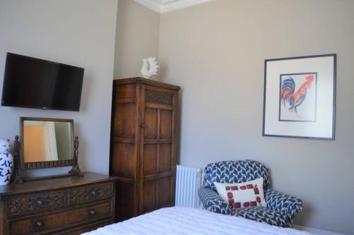 a bedroom with a tv and a chair and a dresser at Cockloft Romantic Countryside Hideaway in Bishops Cannings
