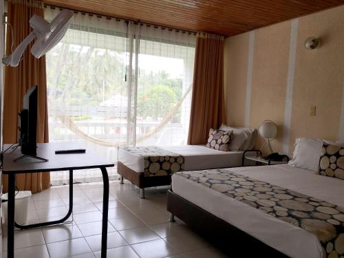 a bedroom with two beds and a desk and a window at Hotel Hacienda El Diamante in Villeta