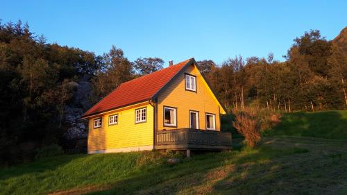 a yellow house with a red roof on a hill at Eimind Feriehus in Eidmind