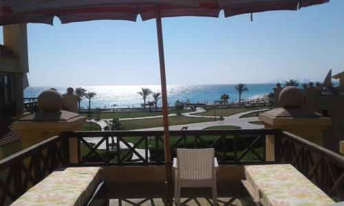 a balcony with two chairs and an umbrella and the ocean at Lazorde bay Sidi Abd El Rahman لازوردى باى apartment in El Alamein