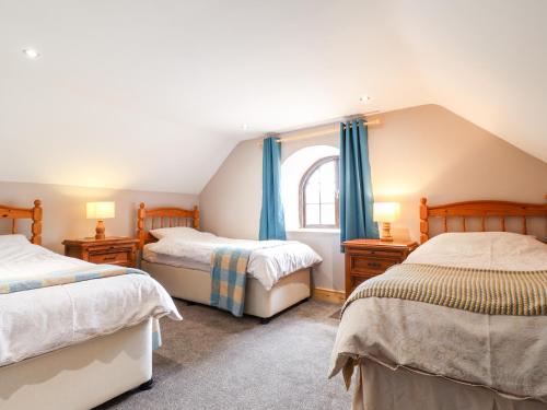 a bedroom with two beds and a window with blue curtains at Barn Court Cottage in Narberth