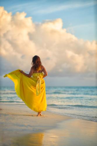 a woman in a yellow dress walking on the beach at PERLA Dhangethi in Dhangethi