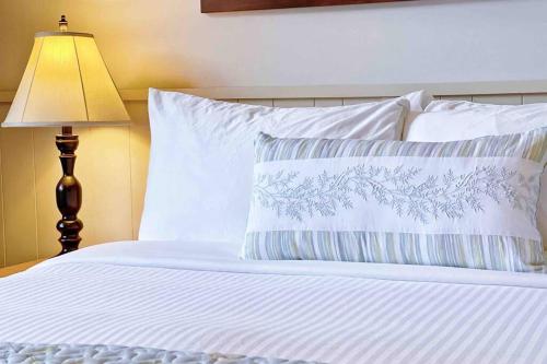 1 cama con sábanas y almohadas blancas y lámpara en Windtower Lodge Queen Bed Suite-UGParking&Walking2DT, en Canmore