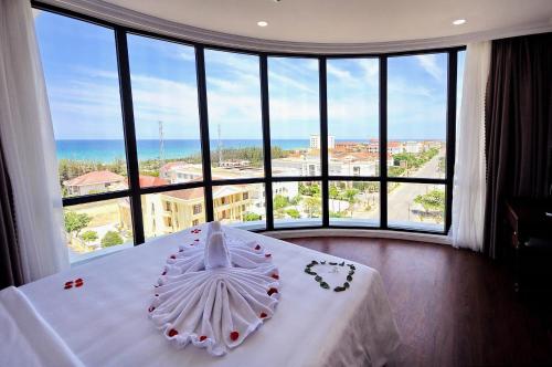 a bedroom with a white bed with a large window at Sunflower Hotel Phú Yên in Tuy Hoa