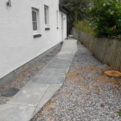 a sidewalk next to a white building with a fence at Loch Ness House Blairbeg in Drumnadrochit
