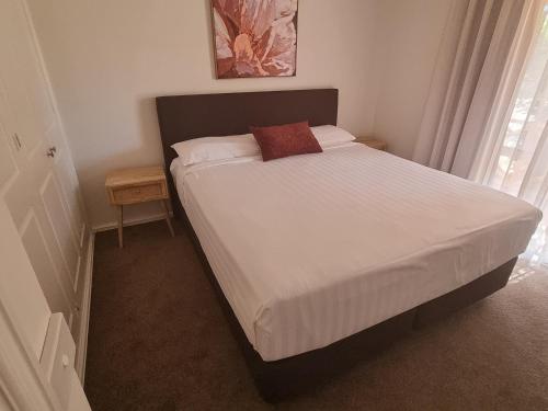 a bedroom with a bed with white sheets and a red pillow at Mildura Holiday Homes - 15th Street in Mildura