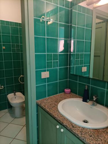 a green tiled bathroom with a sink and a toilet at Casa Mare Cala Rossa in Trinità d'Agultu e Vignola