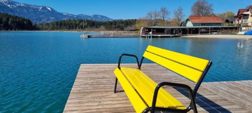 a yellow bench sitting on a dock near the water at Waldschlössl in Latschach ober dem Faakersee