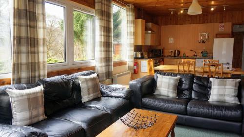 sala de estar con sofás de cuero negro y mesa en Woodland Chestnut Lodge, en Killin