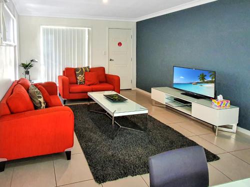 a living room with two red chairs and a flat screen tv at Lillypilly Resort Apartments in Rockhampton