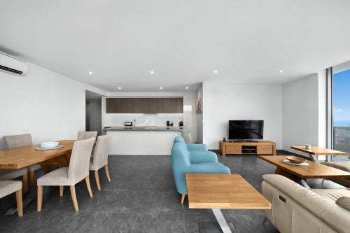 a living room with a blue couch and tables and a kitchen at Luxury Apartment Caves Beach 4 Bed in Caves Beach