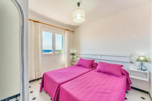 a bedroom with a pink bed with a window at Villas Vanessa & Ruth in Cala en Porter