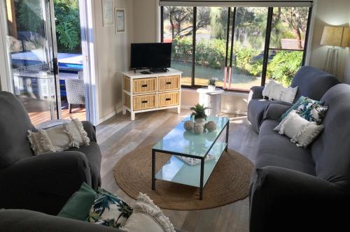 a living room with couches and a tv and a table at SHELLHARBOUR BEACH COTTAGE ---- Back gate onto Beach, Front gate walk to Marina in Shellharbour