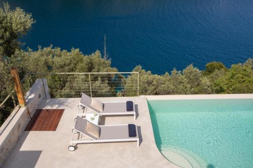 a pool with two lounge chairs next to the water at Villa Anthelia-Idyllic view and private access to the sea in Sivota