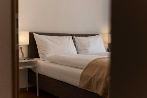 a bedroom with a bed with white pillows and a side table at Montela Apartment-Hotel & Resort in the holiday region Saas-Fee Saastal in Saas-Grund