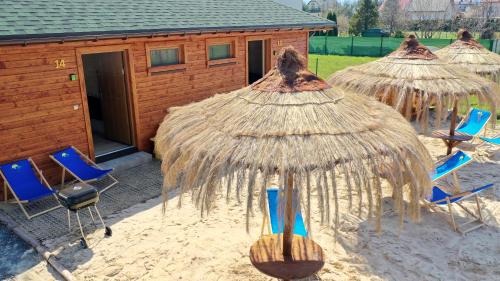a group of straw umbrellas and chairs in the sand at Apartamenty przy Jeziorze Żywieckim z widokiem na Skrzyczne in Żywiec