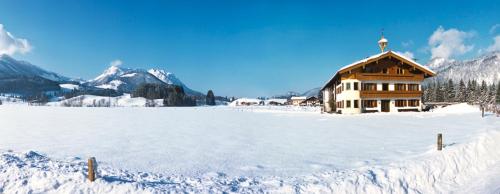 a snow covered field with a house in the distance at Bio-Bauernhof Bachangerhof in Kössen