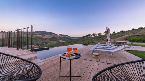 a deck with two glasses of wine and two chairs at Dimora Montefiore 11, Emma Villas in Montefiore dellʼAso
