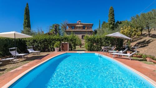 a pool with chairs and umbrellas and a house at PODERINO 6, Emma Villas in Trequanda