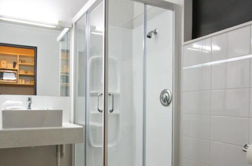 a white bathroom with a shower and a sink at ASURE 83 By The Sea Motor Lodge in Lower Hutt