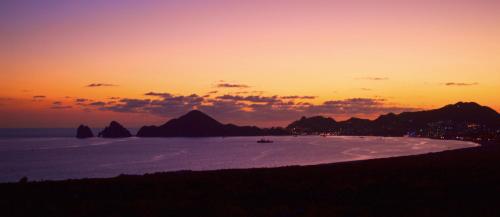 a sunset over a beach with mountains in the background at Sunrock Hotel & Suites in Cabo San Lucas