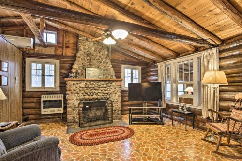 a living room with a stone fireplace and a tv at Lakefront 1930s Log Cabin with Dock and Fire Pit! in Rice Lake