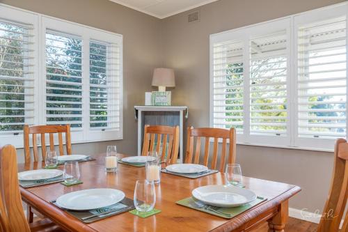 a dining room with a wooden table with chairs and windows at Moruya Holiday House in Moruya