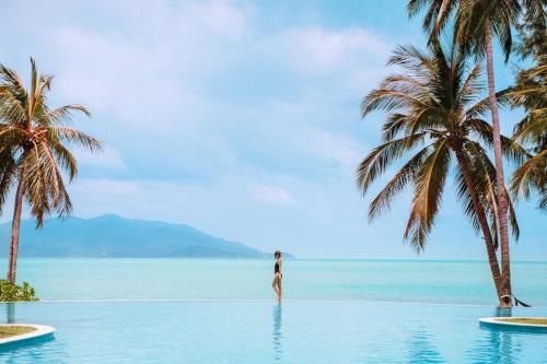 a woman standing in the water at a resort with palm trees at Melati Beach Resort & Spa in Choeng Mon Beach