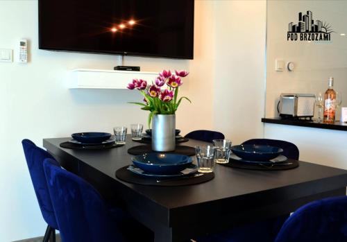 a black table with blue chairs and a vase of flowers at Pod Brzozami Apartamenty 5 Mórz in Ustronie Morskie