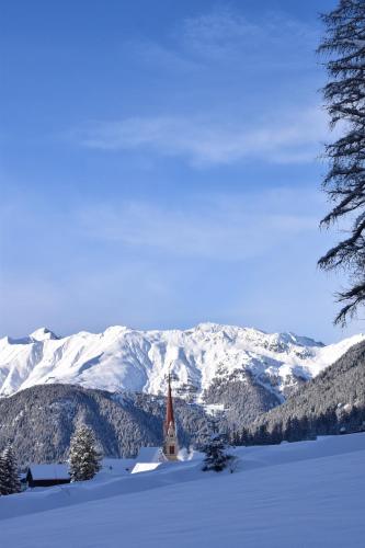 a small church in the snow with snow covered mountains at Penserhof - Alpine Hotel & Restaurant in Sarntal