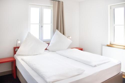 a white bed with white pillows in a room with windows at KU Hotel by WMM Hotels in Kulmbach