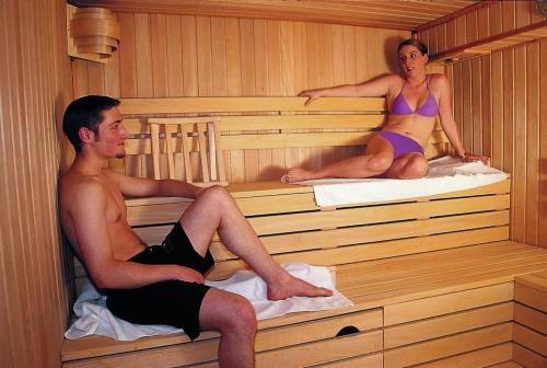 Ein Mann und eine Frau sitzen in einer Sauna in der Unterkunft Parkhotel Kevelaer in Kevelaer