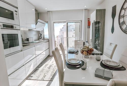 a white kitchen with a table with chairs and a counter at Apartment Rocha Vista Mar Dubai in Portimão