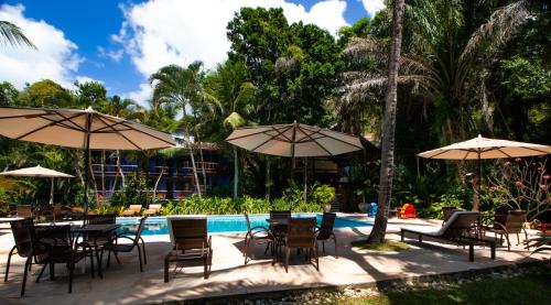 a group of tables and chairs with umbrellas next to a pool at Atmosphera Pousada in Arraial d'Ajuda