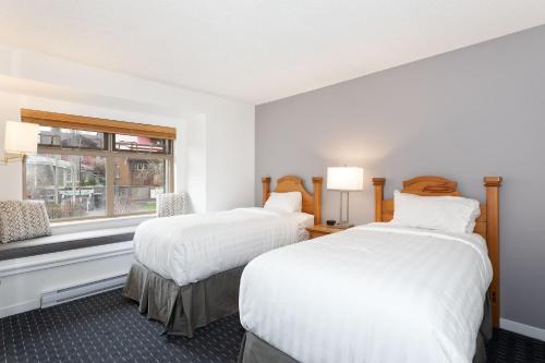 two beds in a white room with a window at Lake Placid Lodge by Whiski Jack in Whistler